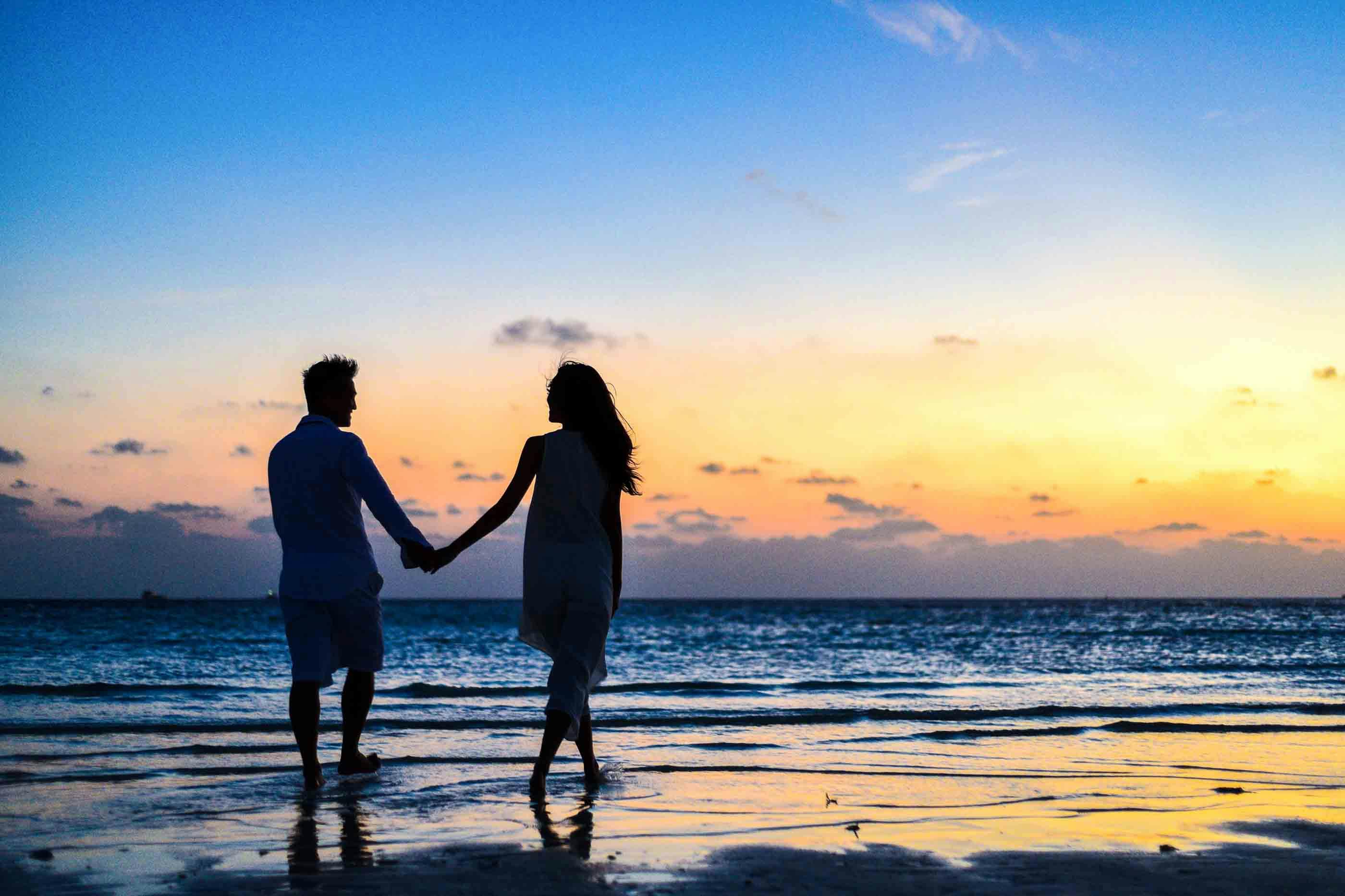 Couple walking together on beach at sunset